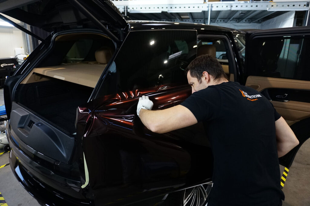 Detailarbeiten beim Carwrapping eines Range Rover in Schwarzrot Glanz – seitliche Ansicht des Hecks während der Verarbeitung durch ACTIV Folientechnik in Kernen bei Stuttgart.
